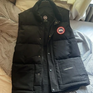 Svart dunväst från Canada Goose - Säljer en svart dunväst från Canada Goose, gammal jacka i ganska bra sick, kan gå ner i pris vid snabb och smidig affär, den är äkta ej med kvitto eller något men det finns qr kod i den och är perfekt till vintern 
