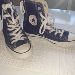 Blå Converse All Star high-top sneakers - Klassiska blå Converse All Star high-top sneakers med vit tå, vita snören och sula. Ikonisk logga på sidan och kontrastsömmar. Skorna är i canvas och har rund tå och platt sula – perfekta för en cool och avslappnad stil. Limited edition