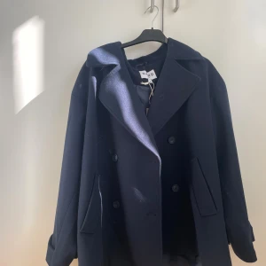 Mörkblå kappa från NA-KD, stl 38 - Snygg mörkblå kappa från NA-KD i klassisk modell med dubbelknäppning och bred krage. Jackan har raka fickor och är perfekt för dig som gillar stilrena och tidlösa plagg. Passar dig som vill ha en enkel men trendig look.