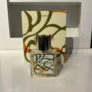 Nishane Papilefiko - Unik parfym från Nishane, Papilefiko Extrait de Parfum. Flaskan är fyrkantig i genomskinligt glas med en stilren, silverfärgad metallkork. Etiketten har gröna och orange mönster och parfymen kommer i en matchande ask. Doften är exklusiv och modern.