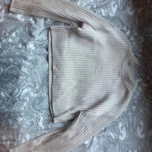 Beige ribbstickad tröja från H&M XS - Säljer en beige ribbstickad tröja från H&M i storlek XS. Tröjan har lång ärm, rund halsringning och är i ett mjukt stickat material. Perfekt för lager-på-lager och enkel att matcha med jeans eller kjol.