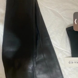 Svarta skinnbyxor från NA-KD - Snygga svarta läderbyxor i skinnimitation från NA-KD. De har utsvängda ben, hög midja och stängs med knapp och dragkedja. Perfekta för en trendig look och lätta att matcha med olika outfits.