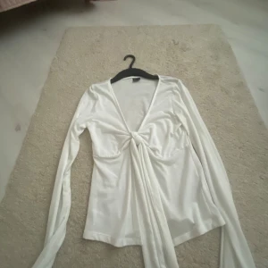 Vit omlottopp från Gina Tricot - Säljer en vit omlottopp från Gina Tricot i storlek S. Toppen har långa ärmar, v-ringning och en snygg knytning framtill som ger en trendig look. Perfekt att styla med jeans eller kjol för en fräsch outfit.