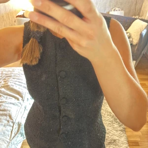 Svart glittrig tweedväst från H&M Divided - Snygg svart väst i tweed från H&M Divided. Västen har rund halsringning, markerad midja och knäppning med tygklädda knappar framtill. Materialet är strukturerat och ger en cool, dressad vibe med glittertrådar som gör toppen mer uppklädd! En perfekt top till nyår eller ett festligare tillfälle!