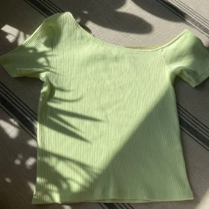 Ljusgrön ribbad topp från Zara - Superfin ljusgrön ribbad topp från Zara med kort ärm och lätt asymmetrisk halsringning. Toppens material är mjukt och stretchigt, perfekt för en chill och trendig look. Enkel att matcha med jeans eller kjol för en fräsch vibe.