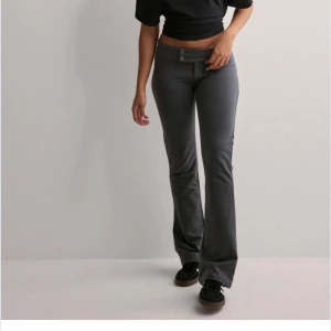 Lågmidjade gråa kostymbyxor  - Snygga mörkgrå byxor med bootcut och två knappar i midjan. Byxorna har låg midja och är tillverkade i ett mjukt, stretchigt material som sitter skönt. Perfekta för dig som gillar en stilren och trendig look.