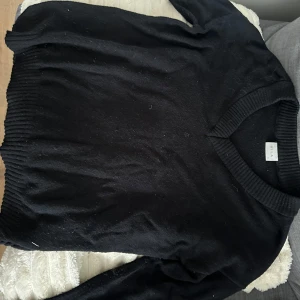 Svart v-ringad tröja från Vila - Svart stickad v-ringad tröja från Vila i mjukt material. Tröjan har långa ärmar, bred ribbstickad mudd vid ärmslut och nederkant samt en klassisk passform. 