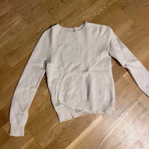 Beige stickad tröja med rund hals - En stilren beige stickad tröja med rund halsringning och långa ärmar. Tröjan har ribbade muddar vid ärmslut och nederkant, vilket ger en snygg och enkel look. Perfekt för lager-på-lager och passar till många olika outfits.