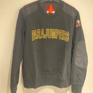 Svart fleece-tröja Parajumpers  - Svart långärmad fleece-tröja från Parajumpers i storlek XL. Skulle dock säga att den passar bättre för dem som har storlek L då den inte är en XL enligt mig. Köpt på NK i Göteborg .Tröjan har gula bokstäver på bröstet, quiltade detaljer på axlar och armbågar samt en patch på ena ärmen. Perfekt för dig som gillar streetwear och vill ha något bekvämt och snyggt.
