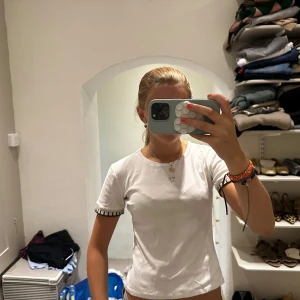 Vit t-shirt från Zara - Säljer en vit t-shirt med korta ärmar och rund hals. Ärmsluten har snygga pärldetaljer i vitt och svart som ger en unik touch. T-shirten har en normal passform och är gjord i mjuk bomull, perfekt för en chill och stilren look.