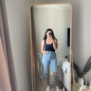 Mom jeans med hål från Stradivarius - Säljer ett par ljusblå mom jeans från Stradivarius i storlek 38. Modellen är högmidjad och slim fit med raka ben och slitna hål vid knäna. Klassisk femficksdesign och tillverkade i bomull. Perfekt för dig som gillar en chill och trendig look.