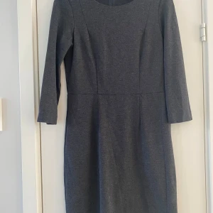 Mörkgrå klänning från Part Two - Snygg mörkgrå klänning från Part Two i storlek L. Modellen har trekvartsärm, rund halsringning och en rak, enkel siluett. Perfekt för dig som gillar stilrena och klassiska plagg. Materialet känns mjukt och bekvämt mot huden.