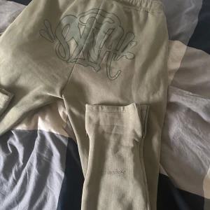 Olivgröna mjukisbyxor med tryck - Snygga olivgröna mjukisbyxor med ett coolt tryck på baksidan och texten 'Forgive Me' på benet. Byxorna har en elastisk midja med dragsko för extra komfort.