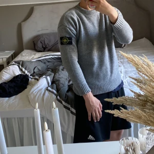 Grå stickad Stone Island tröja - Säljer en grå stickad tröja från Stone Island med klassisk patch på vänster ärm. Tröjan har rund halsringning, ribbade muddar och är långärmad. Perfekt för dig som gillar stilren och enkel design med streetwear-vibe. (Tyvärr inte äkta)