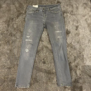 Grå jeans från Dondup, - Säljer ett par grå skinny jeans från Dondup i storlek 29. Jeansen har slitna detaljer framtill, klassiska fem fickor och läderpatch med logga bak. Snygg tvätt och smal passform som sitter tajt hela vägen ner. Fickorna är väldigt små 