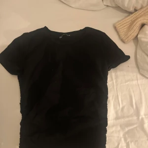 Svart basic t-shirt - En enkel svart t-shirt med rund hals och korta ärmar. Perfekt att matcha med jeans eller kjol för en clean look. T-shirten har en klassisk passform och är gjord i mjukt material som känns skönt mot huden. Detaljer på sidorna 