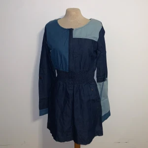 Kort jeansklänning med dragkedja - Snygg kort klänning i jeansmaterial med patchwork i olika blå nyanser. Klänningen har långärmade ärmar, markerad midja med smock och dragkedja framtill. Fickor med knappdetaljer och cool kontrast mellan mörkblått och ljusblått tyg gör den unik och trendig.