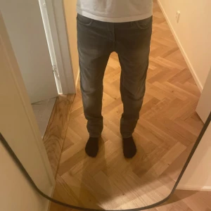 Grå straight jeans från Jack & Jones - Säljer ett par gråa jeans från Jack & Jones med klassisk femficksdesign och slim/straight passform. Jeansen har normal midja och är tillverkade i slitstarkt denim. Perfekta för dig som gillar en enkel och clean look med lite faded effekt på benen. Storleken är W29 L30 och modellen heter Tim slim/straight