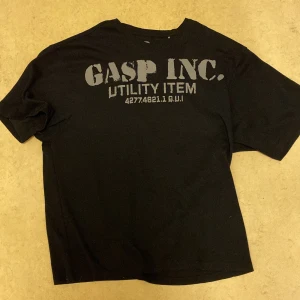 Svart GASP t-shirt med tryck - Svart t-shirt från GASP med stort grått tryck både fram och bak. Modellen är klassisk med rund hals och korta ärmar. Materialet är mjuk bomull som känns skön mot huden. Perfekt för dig som gillar sportig och street-inspirerad stil.