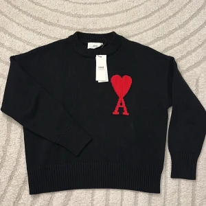 Ami Paris Tröja  - Ami Paris tröja Helt ny och aldrig använd, alla taggar sitter fortfarande kvar! Tyvärr för liten för mig, så säljer den vidare. Klassisk svart design med rött hjärta och “A”-logo framtill ❤️  💸 Pris: 749 kr 🔥 Perfekt chans att få en exklusiv tröja till bra pris! 