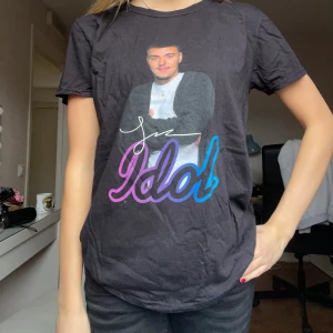 Svart Idol t-shirt - Cool svart t-shirt med Idol-tryck i lila och blått framtill samt bild på Joel som kom 2:a i idol 2024😍Klassisk rund hals och korta ärmar. Perfekt för dig som gillar Idol och vill sticka ut med ett färgglatt motiv. Skön passform och mjukt material. Köpte för 249kr och säljer för 100kr!