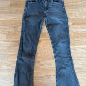 Grå bootcut jeans från Gina Tricot - Snygga grå jeans från Gina Tricot med bootcut-modell och klassisk femficksdesign. Jeansen har en mörkgrå tvätt och är tillverkade i mjukt denimtyg med dragkedja och knapp framtill. Perfekta för dig som gillar en retroinspirerad look. OBS! Det är barnstorlek men är i fint skick.