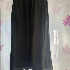 Mörkgrön långkjol med snörning - Mörkgrön långkjol med snygg snörning i midjan. Kjolen har ett lätt, flowy tyg med subtila ränder i strukturen som ger en cool och avslappnad vibe. Perfekt för dig som gillar enkel och stilren design med en twist.