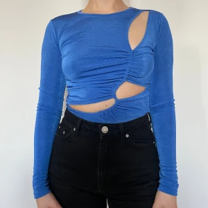 Blå cut out topp från Pull&Bear - Säljer en blå långärmad topp från Pull&Bear med coola cut out-detaljer och rynkade partier framtill. Toppen är figurnära och har en unik design med asymmetriska öppningar. Perfekt för dig som vill sticka ut med din stil.