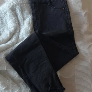 Svarta high waist jeans från Bershka - Säljer ett par svarta high waist jeans från Bershka. De har klassisk femficksdesign, smal passform och råa kanter nertill. Jeansen är i stretchigt denimtyg och har bälteshällor och knappstängning framtill.