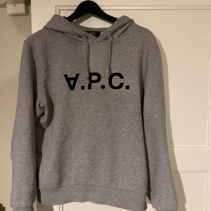 Grå hoodie från A.P.C. med tryck - Säljer en stilren grå hoodie från A.P.C. med svart logotyptryck på bröstet. Tröjan har huva med snörning och lång ärm, perfekt för en chill och avslappnad look. Standard fit och 100% bomull  som känns väldigt bra! (Nypris 3000kr) Snabb affär= bättre priser😁