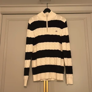 Randig stickad tröja från GANT - Säljer en snygg stickad tröja från GANT i storlek M. Tröjan är näst intill aldrig använd och Tröjan har breda mörkblå och vita ränder, half zip i halsen och kabelstickat mönster. Hör av dig vid funderingar Mvh/Max