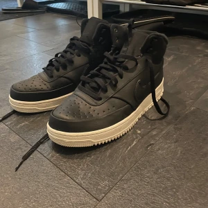 Nike vinterskor - Säljer ett par svarta Nike vinter skor med vit sula. Klassisk siluett med högt skaft, perforerad tå och snörning. Skorna är i skinn och har den ikoniska swoosh-loggan på sidan. Perfekta för dig som gillar att vara varm i vintern och vill ha en clean look. Har använts 2 gånger!!!!