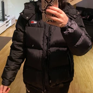 Svart pufferjacka Tommy Jeans - Säljer en svart pufferjacka från Tommy Jeans i modellen The Alaska Puffer. Jackan har huva, dragkedja och klassisk logga på bröstet. Perfekt för kalla dagar under vintern och riktigt skön passform. Endast använd ett par gånger, då jag köpte en ny, pris kan diskuteras. Köpt för 2899😊