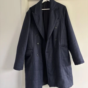 Mörkblå ullrock från Morris, strl 48 - Snygg mörkblå rock från Morris Heritage med dubbelknäppning och breda slag. Tillverkad i 100% ull med foder i viskos. Klassisk design med fickor och knappar vid ärmslut, perfekt för dig som gillar stilrena och tidlösa plagg.