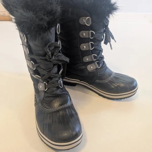 Svarta vinterboots Sorel - Snygga och väldigt bekväma vinterboots med snörning och quiltad ovandel. Skorna har fuskpäls upptill och är varmfodrade, grov sula och detaljer i skinn och syntet. Perfekta för kalla dagar.