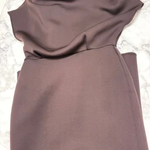 Brun klänning från ASOS DESIGN - Snygg brun klänning från ASOS DESIGN i stilren modell med slits framtill. Klänningen har en enkel, elegant design och är tillverkad i ett mjukt, följsamt material som ger en lyxig känsla. Perfekt för dig som gillar minimalistisk stil och vill sticka ut med en jordnära färg.