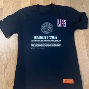 t-shirt Heron Preston  - Svart t-shirt från Heron Preston med  tryck 'INFLUENCER JETSTREAM' Rosa LIFE-tryck på bröstet och ryggen, samt broderad text på ärmen. Orange Heron Preston-label nedtill. Skön passform och tillverkad i mjuk bomull. Pris kan diskuteras 