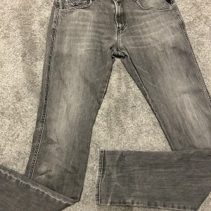 Replay Anbass grå jeans, 30/34 - Snygga Replay Anbass jeans i tvättad grå färg med svarta sömmar och klassiska fem fickor. Modellen har raka ben och normal passform, tillverkade i mjukt jeanstyg. Bakfickorna har Replay-logga och coola broderade detaljer. (Som ni kan se i bild 2 så finns det ett jätte litet hål precis under gylfen) skriv vid funderingar 