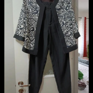 Svart och vit mönstrad kostym - Snygg kostym med svart byxa och kavaj i svart och vitt med unikt snirkligt mönster. Kavajen har vida ärmar och kontrasterande svarta kanter. Passformen är normal och materialet känns som polyester. Perfekt för dig som vill sticka ut med en cool look.