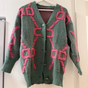 Grön kofta med rosa mönster från SHEIN - Grön stickad kofta från SHEIN med unikt rosa mönster och stora knappar framtill. Koftan har lång ärm, ribbade muddar och oversized känsla. Perfekt för dig som vill sticka ut med färg och mönster i höst och vinter.