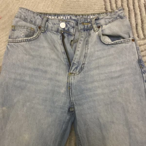 Ljusblå straight split jeans från UO - Säljer ett par ljusblå jeans från Urban Outfitters med straight split-modell. Byxorna har hög midja, klassiska fem fickor och en snygg slits nertill på benen. Tillverkade i jeansmaterial med kontrastsömmar och läderpatch bak.
