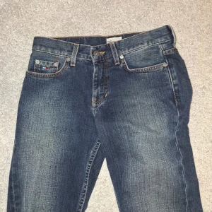 Blå bootcut jeans från Tommy Hilfiger - Snygga blå jeans från Tommy Hilfiger med klassisk femficksdesign och bootcut-ben. Jeansen har en mörk tvätt med lätt slitning på låren och bakfickor med diskret logga. Perfekta för dig som gillar en avslappnad men ändå stilren look.PRIS KAN DISKUTERAS.
