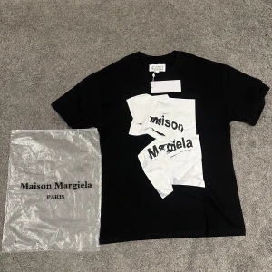Maison Margiela svart t-shirt med print - Maison Margiela svart t-shirt i bomull med korta ärmar och coolt vitt grafiskt print framtill med Maison Margiela-logga. Rund hals och klassisk passform. Levereras med originalpåse från Maison Margiela Paris. Perfekt för dig som gillar designerplagg.