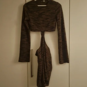 Brun kortklänning med cut-out H&M - Kort brunmelerad klänning från H&M Divided med långa ärmar och coola cut-out detaljer i midjan. Klänningen har en tight passform och är tillverkad i ett mjukt, stretchigt material. Perfekt för dig som gillar trendiga och unika plagg.
