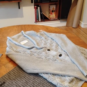 Ljusgrå kofta från These Glory Days - Säljer en ljusgrå stickad kofta från These Glory Days i storlek small. Koftan har snygg kabelstickad design, stora knappar framtill och två fickor. Perfekt för lager-på-lager och chill höst- eller vinterstil.