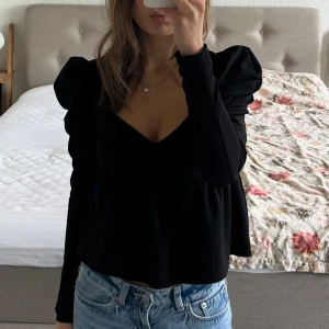 Svart figursydd blus med puffärmar och v-ringning - Säljer en svart blus med puffärmar och insydd midja. Använd fåtal gånger. 