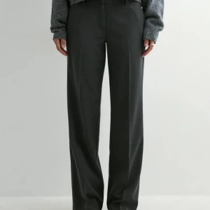 Mörkgrå lågmidjade kostymbyxor från Nelly - Snygga mörkgrå kostymbyxor från Nelly i rak modell. Byxorna har låg midja, pressveck fram och bak, bälteshällor och fickor i sidorna. Storlek 40 och passar mig som är 180cm lång. 