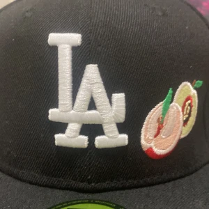 LA Dodgers 59FIFTY keps World Series - Svart 59FIFTY keps från New Era med LA Dodgers brodyr framtill, färgglada fruktmotiv och texten 'Do it for the culture' i regnbågsfärger på sidan. Broderad World Series 1988-logga och MLB-märke. Klassisk flat peak och strukturerad passform.