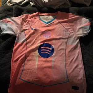 Barça Nike fotbollströja rosa/blå S - Barcelona fotbollströja från Nike i Dri-Fit ADV-material. Tröjan är rosa med blå detaljer och har klubbmärke, Nike-logga och Spotify som sponsortryck. V-ringad krage med blå kant och korta ärmar. Perfekt för dig som älskar fotboll och vill sticka ut på planen.