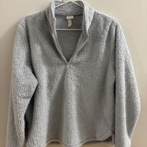 Ljusgrå fleece-tröja med half zip - Supermjuk och mysig ljusgrå fleece-tröja från HM. Tröjan har en halv dragkedja framtill och långärmad design. Perfekt för kyliga dagar när du vill vara både bekväm och snygg.